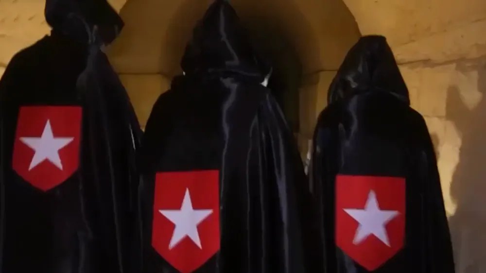 Tempeleers in zwart habijt met puntmuts gefilmd